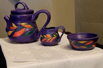 Blue violet teapot with carved coral, yellow, green floral design, creamer and sugar bowl